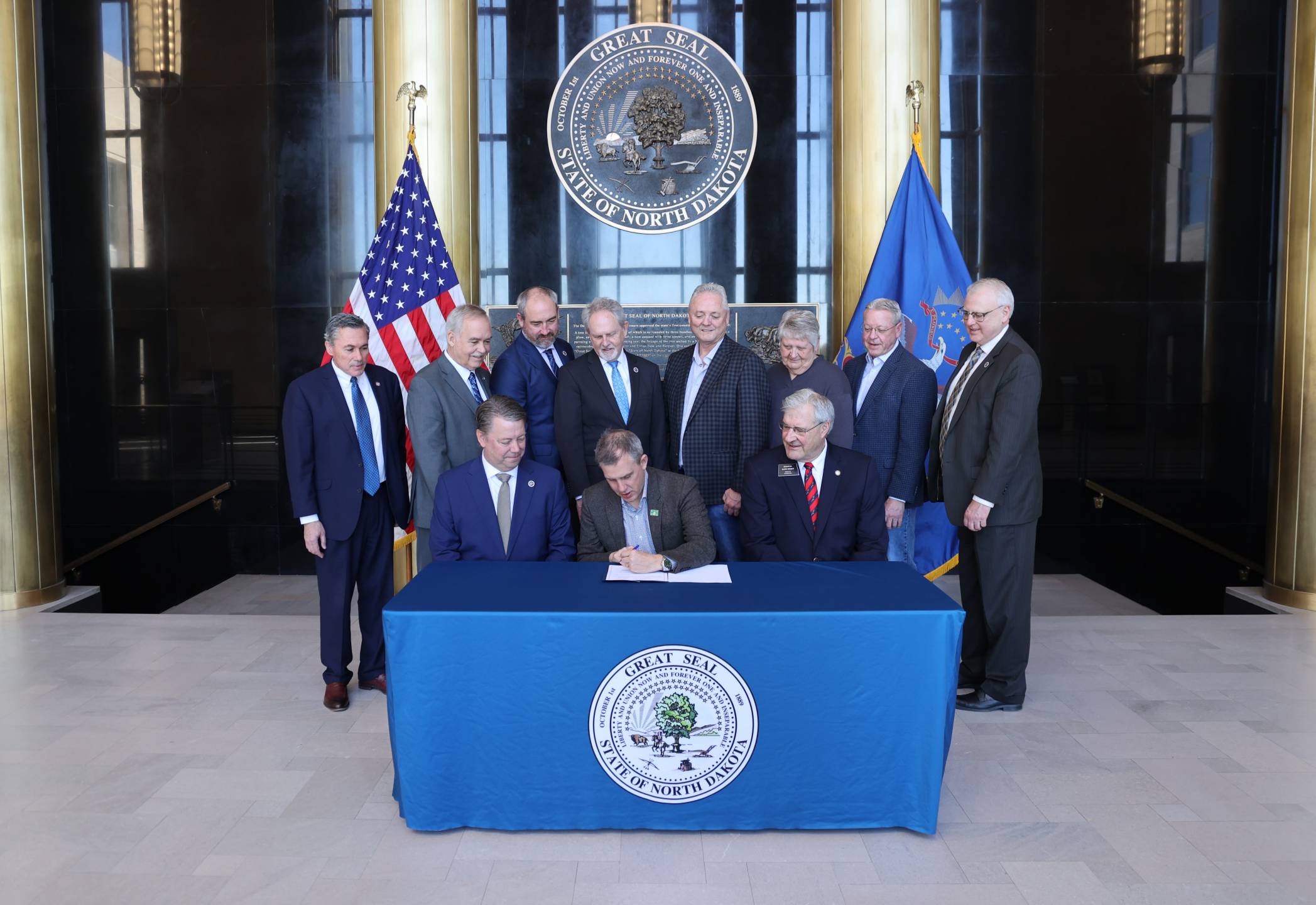 Gov. Armstrong signs House Bill 1176 in the Capitol's Memorial Hall with legislators watching.